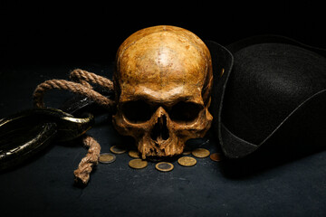 Human skull with sword, toy model of cannon, pirate hat and coins on black background © Pixel-Shot