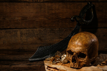 Human skull with sword, old manuscripts and golden nuggets on brown wooden background