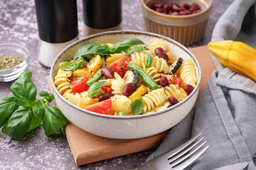 Bowl of tasty pasta salad with tomatoes and basil on dark table