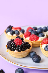 Plate of tasty tartlets with whipped cream and berries on lilac background