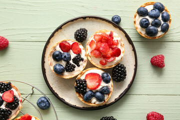 Plate of tasty tartlets with whipped cream and berries on green wooden background