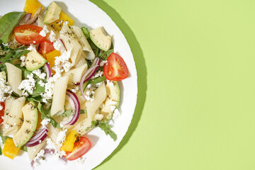 Plate of tasty pasta salad with tomatoes and avocado on green background