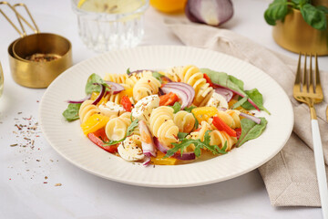 Plate of tasty pasta salad with pepper and red onion on white background
