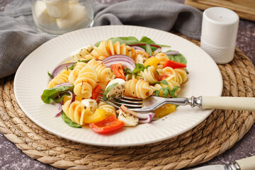 Plate of tasty pasta salad with pepper and red onion on dark table