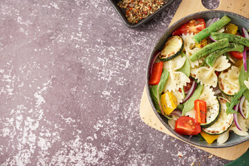 Bowl of tasty pasta salad with pepper and red onion on dark background