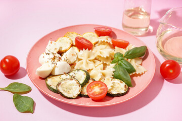 Plate of tasty pasta salad with tomatoes and basil on pink background