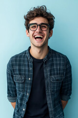 Fototapeta premium Young Caucasian man with glasses, smiling with energy and enthusiasm, standing against a light blue background, showing excitement and approachability.
