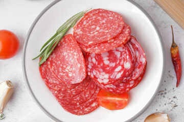 Plate with slices of tasty salami on light background