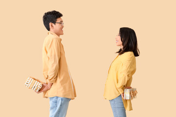 Young Asian friends greeting each other with gifts on beige background