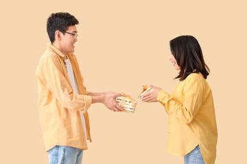 Young Asian friends greeting each other with gifts on beige background