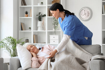 Female nurse caring about lying senior woman at home