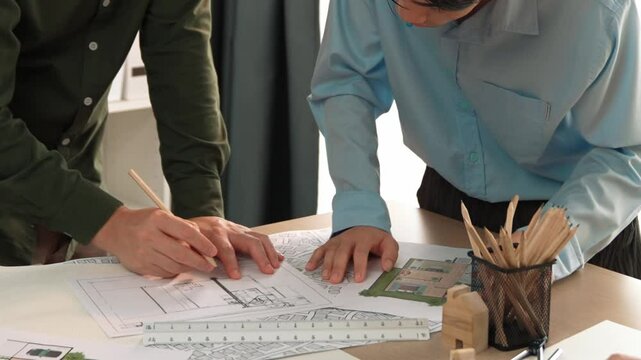 Smart architect and safety engineer discussion about building blueprint on table with architectural document, measurement tools and wooden block scatter around at modern office. Closeup. Delineation.