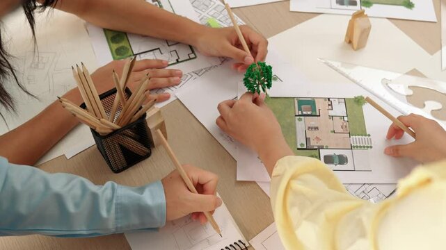 Architect and engineer use tree model discuss about building blueprint on table with architectural document, measurement tools and wooden block scatter around at modern office. Closeup. Delineation.
