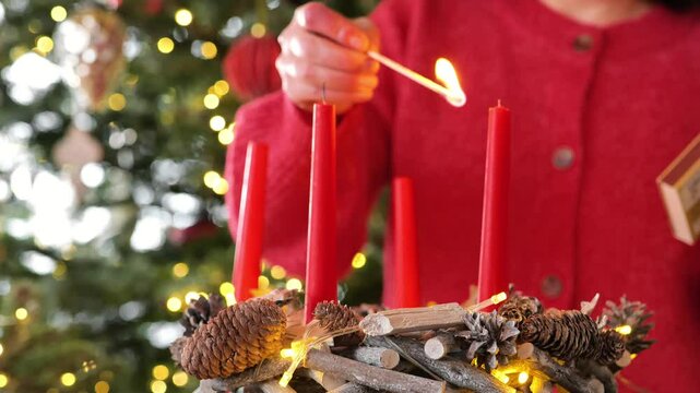 First Advent. Christmas wreath with four red candles.First week of Christmas. Woman lights first candle of Advent wreath on Christmas beautiful tree background.Christmas traditions and customs