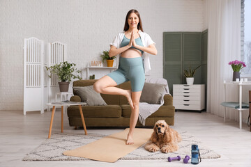 Sporty young pregnant woman with cocker spaniel meditating at home