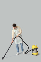 Young man with vacuum cleaner on light background