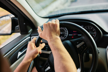 Naklejka premium Hands gripping the steering wheel of a car while driving on a road