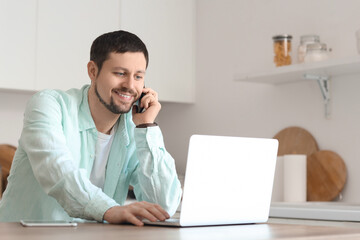 Young male teacher with laptop and mobile phone giving online lesson at home
