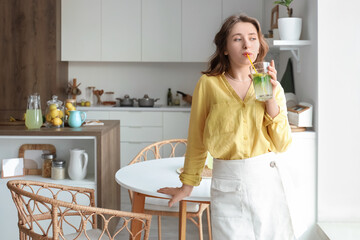 Young woman drinking tasty lemonade in kitchen