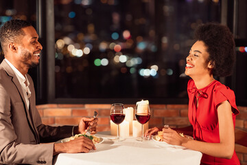 Dating Romance. Loving Afro Couple Celebrating Valentine Having Dinner, Laughing And Talking In Restaurant.