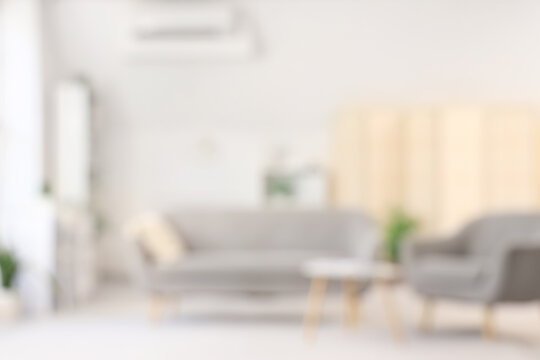 Blurred view of light living room with grey sofa, armchair and table