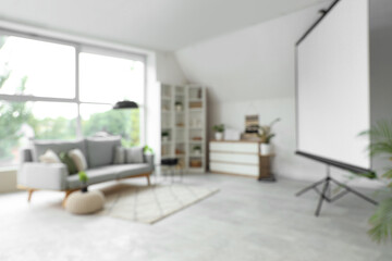 Blurred view of light living room with sofa and projector screen
