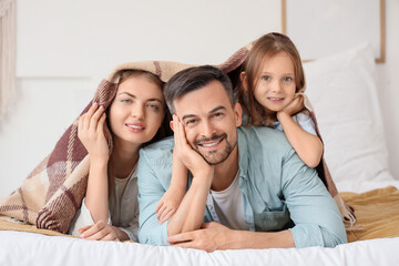 Little girl and her parents lying under warm plaid in bedroom