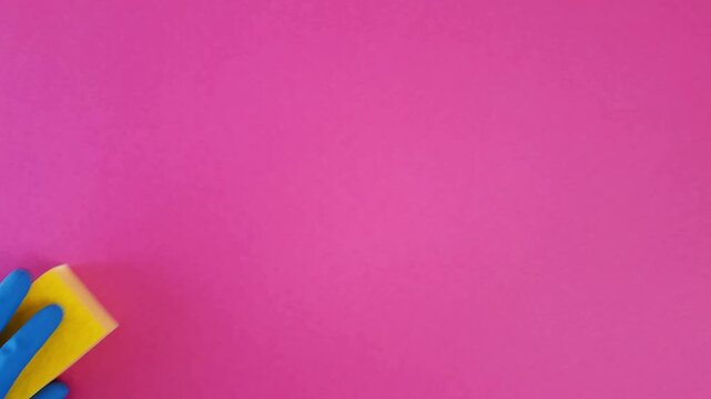 Hand in blue rubber glove picks up yellow kitchen sponge from pink table. Cleaner takes cleaning product. Housewife cleaning, household to-do list, timetable and schedule housework concept.