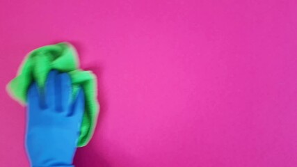 Person wipes pink wall. Close-up of a staff cleaner's hand with green rag. Rubber glove and microfiber cloth during cleaning process. Template with space for advertisement text, message, design