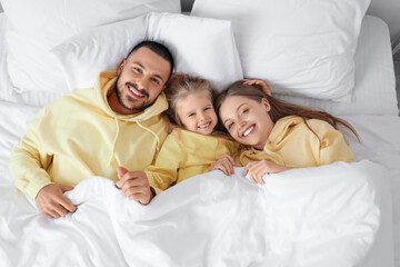 Happy parents with their little daughter lying under blanket on bed, top view