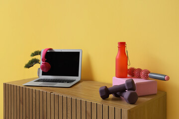 Laptop with headphones and sports equipment on commode near yellow wall