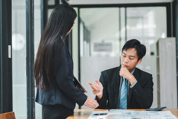 Professional business meeting in a modern office with two Asian colleagues discussing documents and strategies.