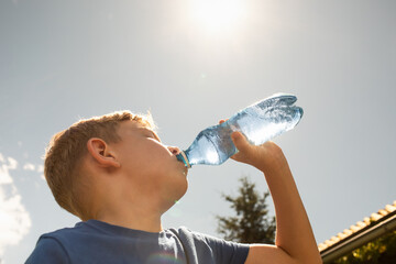 Child drinking water from bottle on a hot summer day, thirsty little boy drinks from water bottle...