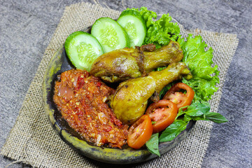 Ayam penyet (smashed fried chicken) is Indonesian East Javanese cuisine, served with sambal chili, lettuce and cucumber slice. Indonesian Spicy Chicken with Various Vegetable