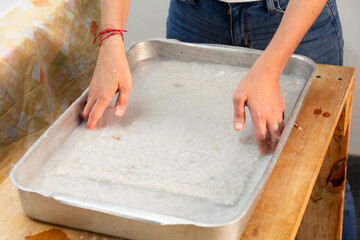 Close-up of unrecognizable woman hands using a deckle in the process of recycling paper in an indoors workshop. Eco friendly and zero waste concept.