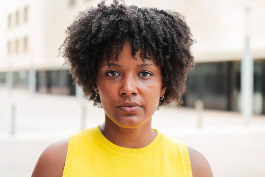 Close up individual portrait of one serious teenage african american girl looking at camera outside. A pensive young adult woman staring front . Proud afro female gazing with thoughtfull expression
