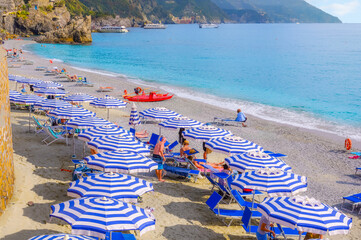 The sandy beach at Monterosso Al Mare, Cinque Terre Italy, with blue and white striped umbrellas,...