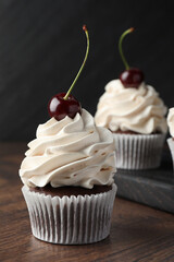 Delicious cupcakes with cream and cherries on wooden table, closeup