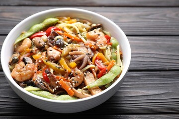 Stir-fry noodles with sea food in bowl on wooden table, closeup