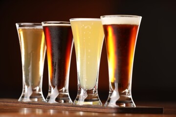 Glasses with different types of beer on wooden table against color background, closeup