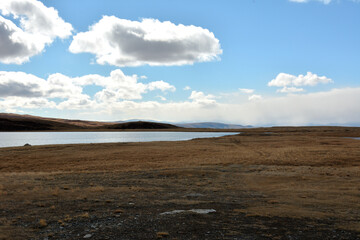 A fragment of a large lake in a flat steppe surrounded by high hills under a cloudy autumn sky.