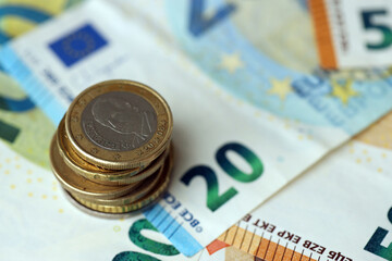 One euro coin lies on huge amount of different euro dollars banknotes