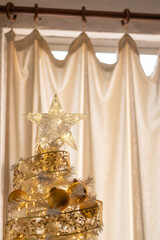 árbol de navidad con decoraciones doradas con estrella en la punta en interior de departamento con...