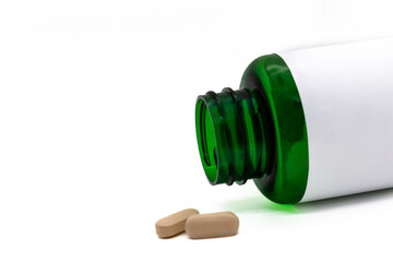 Medicinal vitamin tablets isolated on white background, green medicine bottle with blank label, copy space, selective focus
