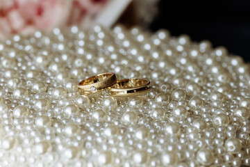 Two gold wedding rings are placed on a bed of white pearls. The pearls are scattered all over the surface, creating a sense of luxury and elegance. The rings are the main focus of the image