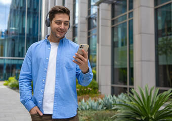 Smiling Young Man Using Smartphone Outdoors Near Modern Office Building