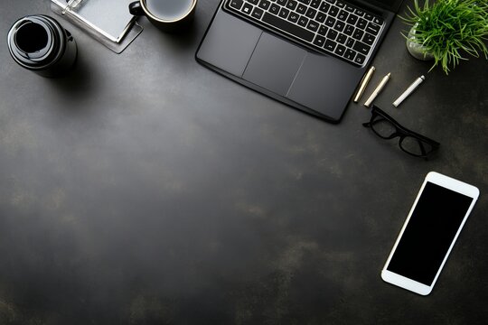 A neatly organized modern workspace featuring a laptop, smartphone, glasses, coffee, and stationery on a dark desk.