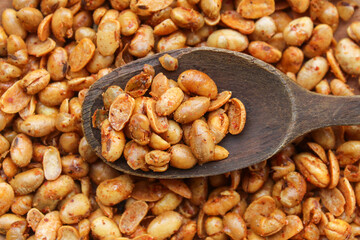 close up of peanuts with spicy seasoning on wooden spoon. background on pile of peanuts. peanut snack