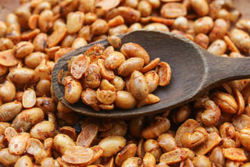 close up of peanuts with spicy seasoning on wooden spoon. background on pile of peanuts. peanut snack
