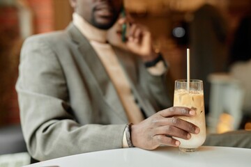 Blurred man in suit holding phone to ear while gripping iced coffee with straw. Focus is on drink, with person slightly obfuscated in background
